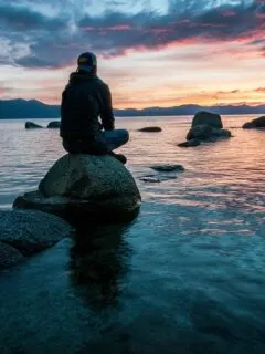 man sitting on rock surrounded by water